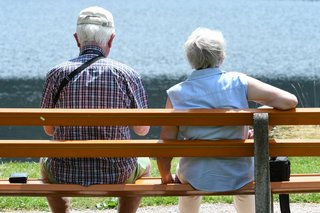 Zwei Rentner sitzen in der Sonne auf einer Bank. 