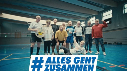 Gruppenfoto einer Volleyballmannschaft, die aus älteren Sportlern besteht, in einer Turnhalle. Darüber das Logo der Aktion Alles geht zusammen.