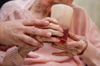 Eine Altenpflegerin hilft einer Seniorin beim Halten eines Trinkbechers. 