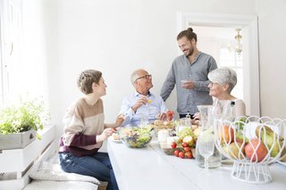 Ein älteres und ein jüngeres Paar an einem reich gedeckten Frühstückstisch, sie unterhalten sich offenbar angeregt. 