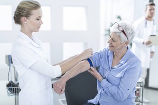 Eine Arzthelferin legt einer Seniorin eine Manschette am Oberarm an, um Blut abzunehmen.