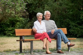 Eine ältere Frau und ein älterer Mann sitzen Arm in Arm auf einer Bank.