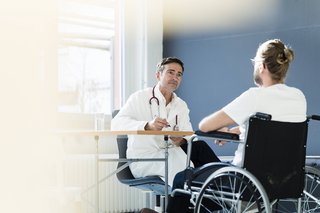 Ein Mann im Rollstuhl sitzt einem Arzt gegenüber.