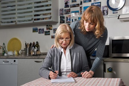 Eine &auml;ltere Frau sitzt an einem Tisch, f&uuml;llt eine VdK-Beitrittserkl&auml;rung aus, eine j&uuml;ngere Frau blickt ihr &uuml;ber die Schulter. 