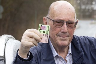 Ein älterer Mann hält seinen Schwerbehindertenausweis mit dem Merkzeichen B hoch. 