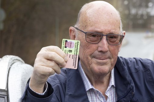 Ein älterer Mann hält seinen Schwerbehindertenausweis mit dem Merkzeichen B hoch. 