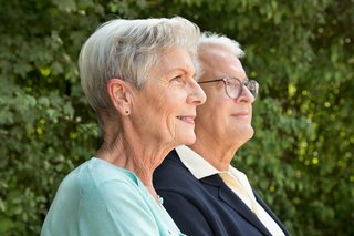 Eine ältere Frau und ein älterer Mann nebeneinander, sie blicken ernst in die Ferne.