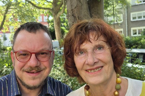 Tim Puffler und sein Mutter Monika Reidegeld nebeneinander drau&szlig;en, sie l&auml;cheln in die Kamera.