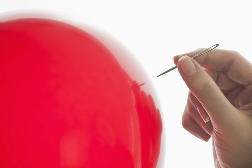 Ein roter Luftballon, eine Hand, die eine Nadel hält, nähert sich.
