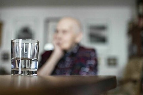 Symbolfoto: Eine alte Frau sitzt allein an einem Tisch, den Kopf auf die Hand gest&uuml;tzt. Im Vordergrund steht ein Wasserglas auf dem Tisch.