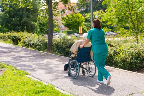 Altenpflegerin mit Dame im Rollstuhl Krankenpflegerin schiebt alte Frau im Rollstuhl