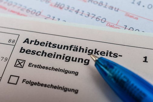 Eine Arbeitsunfähigkeitsbescheinung, auf der "Erstbescheinigung" angekreuzt ist, darauf liegt ein Kugelschreiber