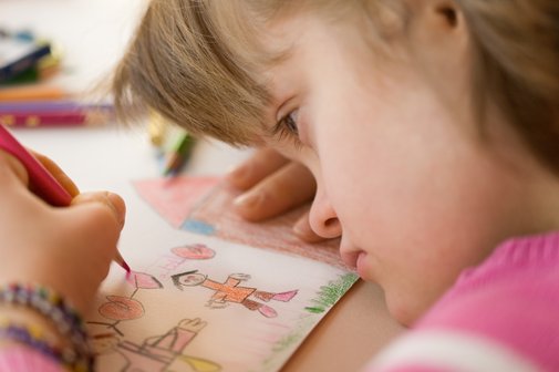 Nahaufnahme eines Mädchens mit Down-Syndrom, das an einem Tisch sitzt und ein Bild malt.