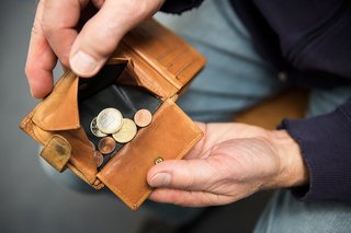 Hände eines Mannes halten eine Geldbörse offen, darin befinden sich wenige Münzen. 