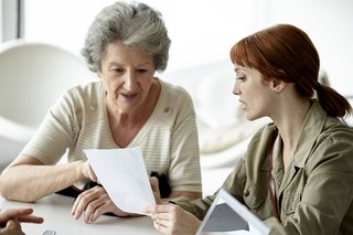  Ältere Frau und jüngere Frau sitzen nebeneinander, besprechen etwas und schauen gemeinsam auf ein Dokument 