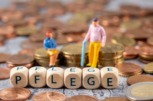 Teure Pflege Seniorenfigürchen sitzen auf Münzstapeln, davor bilden Buchstabenwürfel das Wort Pflege