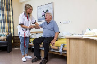 Eine Krankenpflegerin hilft einem älteren Mann beim Aufstehen aus dem Krankenbett.