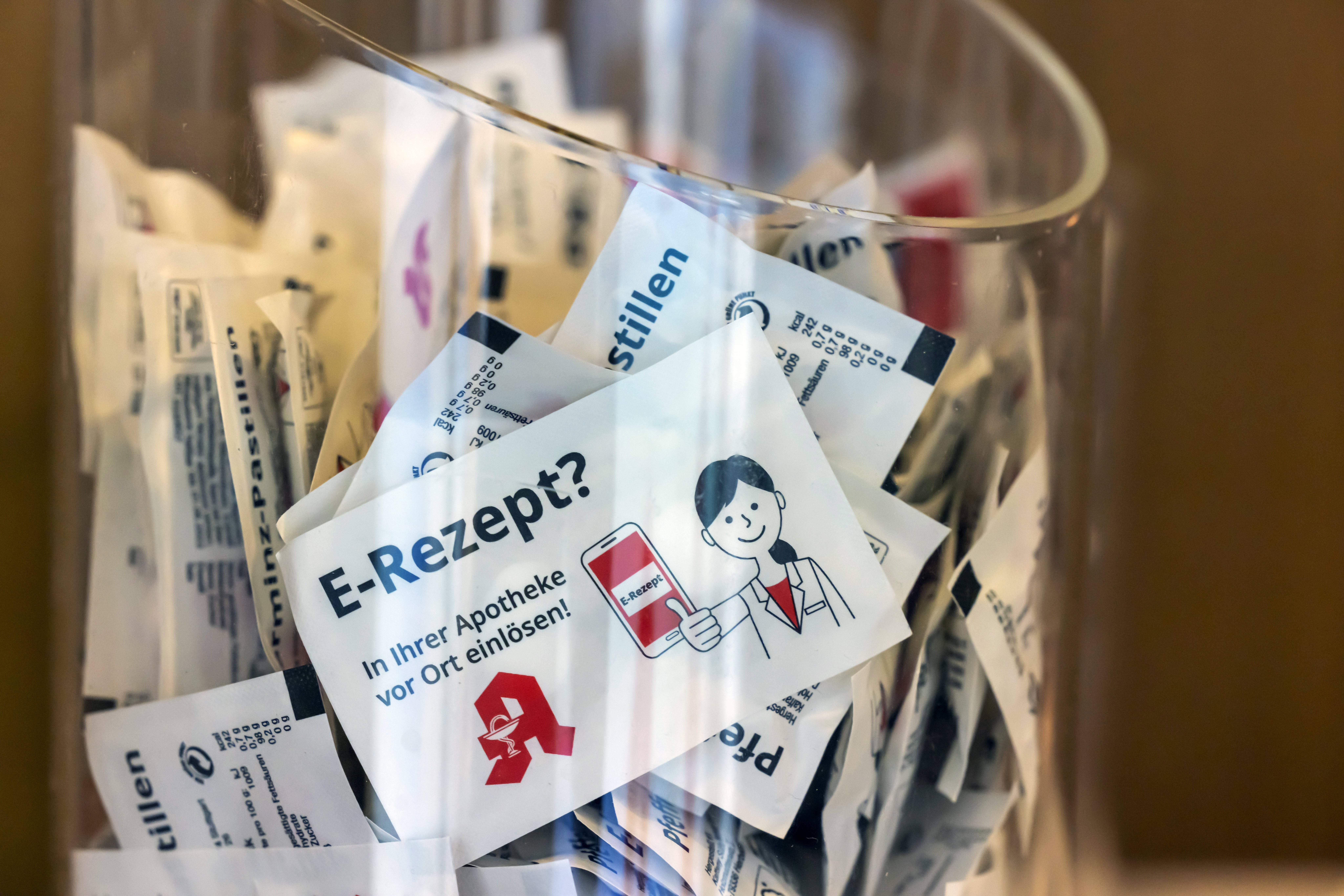Ein gro&szlig;er Glasbeh&auml;lter in einer Apotheke, gef&uuml;llt mit Werbegeschenken mit der Aufschrift "E-Rezept? Vor Ort in Ihrer Apotheke einl&ouml;sen"