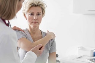 Eine Ärztin untersucht eine Frau, die sich die Schulter hält.