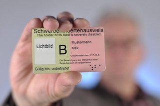 Ein Mann hält einen Schwerbehindertenausweis mit dem Merkzeichen B in die Kamera.