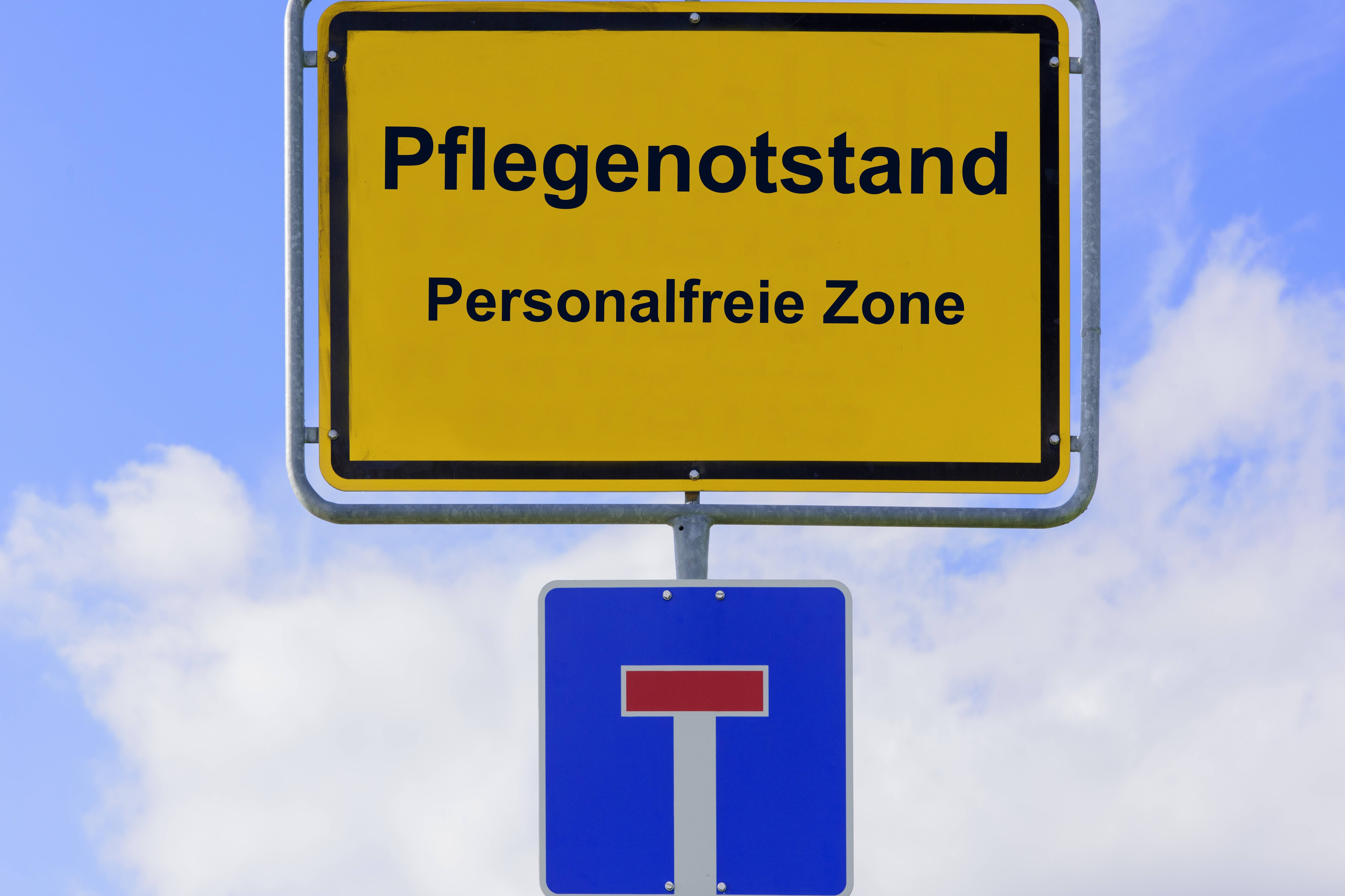 Die Bildmontage zeigt ein Ortsschild mit der Aufschrft "Pflegenotstand. Personalfreie Zone", darunter ist ein Sackgassen-Schild. 