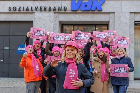 Verena Bentele und viele Mitarbeitende der VdK-Geschäftsstelle in Berlin stehen vor dem VdK-Gebäude, sie halten Schilder der Aktion JASOZIAL hoch.