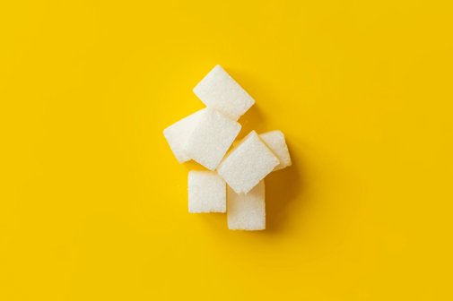 Ein kleiner Berg aus Zuckerwürfeln vor gelbem Hintergrund