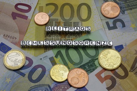 Beitragsbemessungsgrenze Buchstaben-Würfel bilden das Wort Beitragsbemessungsgrenze, die Buchstaben liegen auf Euro-Scheinen und Euro-Münzen