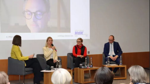 Blick auf das Podium bei der Veranstaltung. Zweite von links ist VdK-Pr&auml;sidentin Verena Bentele, die gerade ins Mikrofon spricht. Per Zoom ist ein weitere Teilnehmer zugeschaltet, den man auf der Beamer-Leinwand sieht. 