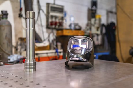 Ein Schweißerhelm auf einem menschenleeren Tisch in einer Fabrik.