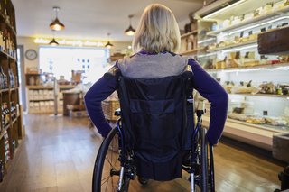 Rückenansicht einer Frau in einem Rollstuhl, die in einem Supermarkt-Gang steht.