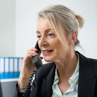 Das Foto zeigt eine Frau an ihrem Schreibtisch. Sie sitzt vor einem Computer und telefoniert.