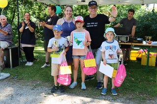 Eine Frau und ein Mann präsentieren drei Kinder mit Urkunden, Pokalen und rosa Turmbeuteln