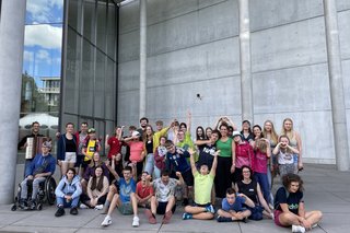 Das Foto zeigt die Teilnehmenden, Begleiterinnen und Begleiter sowie Tänzerin Barbara Galli-Jescheck und den Akkordeonspieler vor der Pinakothek der Moderne.