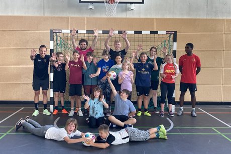 Das Foto zeigt die Teilnehmenden und ihre Betreuerinnen und Betreuer an der inklusiven Ferienfreizeit. Sie stehen in einer Sporthalle vor einem Basketballkorb.