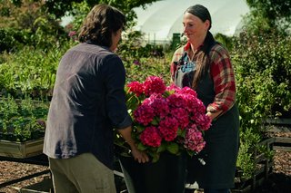 Auf dem Foto ist eine Szene aus dem Werbefilm der Deutschen Rentenversicherung zur medizinischen Rehabilitation zu sehen, in der zwei Frauen einen Blumentopf gemeinsam hochheben..