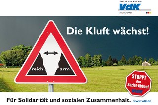 Plakatmotiv für die Bundestagswahl 2013 unter dem Motto "Die Kluft wächst". Darauf steht: Die Kluft wächst! Für Solidarität und sozialen Zusammenhalt. Stoppt den Sozial-Abbau. Im Hintergrund sieht man eine Wiese. Vorne ist ein Warnschild, das zwischen der Kluft zwischen arm und reich warnt.