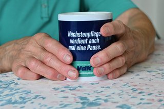 Auf dem Foto sieht man die Hände einer älteren Frau, die eine Tasse in der Hand hält.