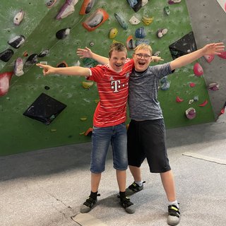Das Foto zeigt Kinder mit Down-Syndrom in einer Boulderhalle. Sie halten sich in den Armen und lächeln in die Kamera. 