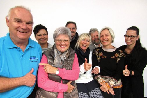 Acht VdK-Ehrenamtliche stehen in zwei Reihen. Sie lachen in die Kamera und geben einen Daumen nach oben. Einer der Ehrenamtlichen tr&auml;gt ein blaues VdK-T-Shirt. Die Ehrenamtliche neben ihm zeigt lachend mit dem Finger auf ihn. 
