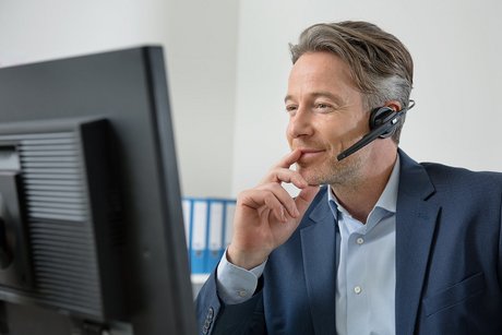 Das Foto zeigt einen Mann an seinem Schreibtisch. Er trägt ein Headset und telefoniert.