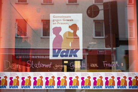 Schaufenster der VdK-Landesgeschäftsstelle. Es hängt ein großes und viele kleine Plakate zum Aktionstag "Gegen Gewalt an Frauen" am Fenster.