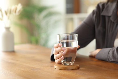 Eine Frau sitzt an einem Tisch und hält ein Glas Wasser in ihrer Hand. 