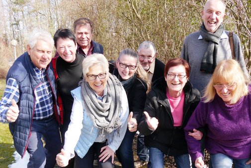 Neun VdK-Ehrenamtliche stehen auf einer Wiese. Im Hintergrund sind kahle B&auml;ume. Sie lachen in die Kamera und geben einen Daumen nach oben. 