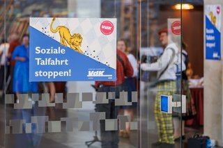 Man sieht das VdK-Plakat zur Landtagswahl 2023 auf einer Glastür. Darauf steht: Soziale Talfahrt stoppen!