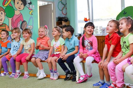 Auf dem Foto sieht man neun Kinder auf zwei Bänken in einer Reihe sitzen.