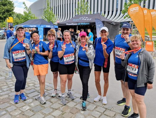 Nach dem Zieleinlauf freuen sich alle über die Medaillen Nach dem Lauf bekamen alle Teilnehmerinnen und Teilnehmer eine Medaille. Auf dem Foto zeigt die Gruppe, die vor einigen Infoständen steht die Medaillen.