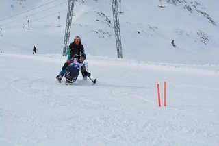 Auf dem Foto sieht man einen Bi-Ski-Teilnehmer in Begleitung auf der Piste.