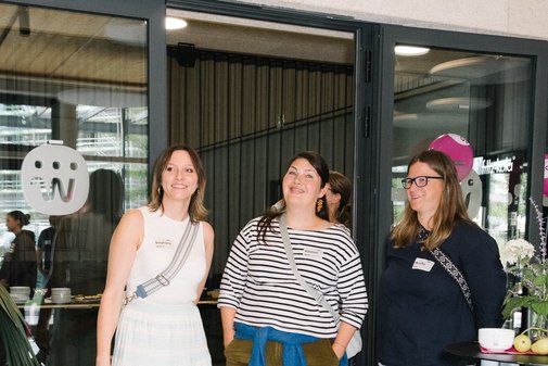 Drei ehemalige Freizeitbegleiterinnen stehen nebeneinander und l&auml;cheln in die Kamera. Sie wurden bei der Feier im Foyer fotografiert.