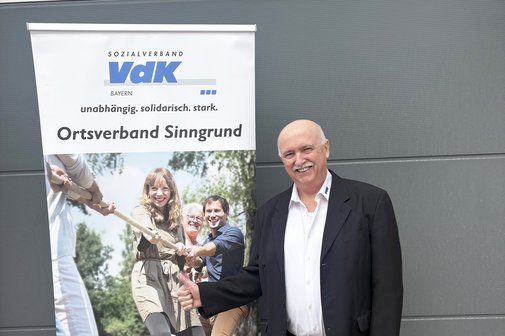 Das Foto zeigt den Ehrenamtlichen Anton Breitenbach vor einem Roll-up des VdK-Ortsverbands Sinngrund. Er l&auml;chelt. 